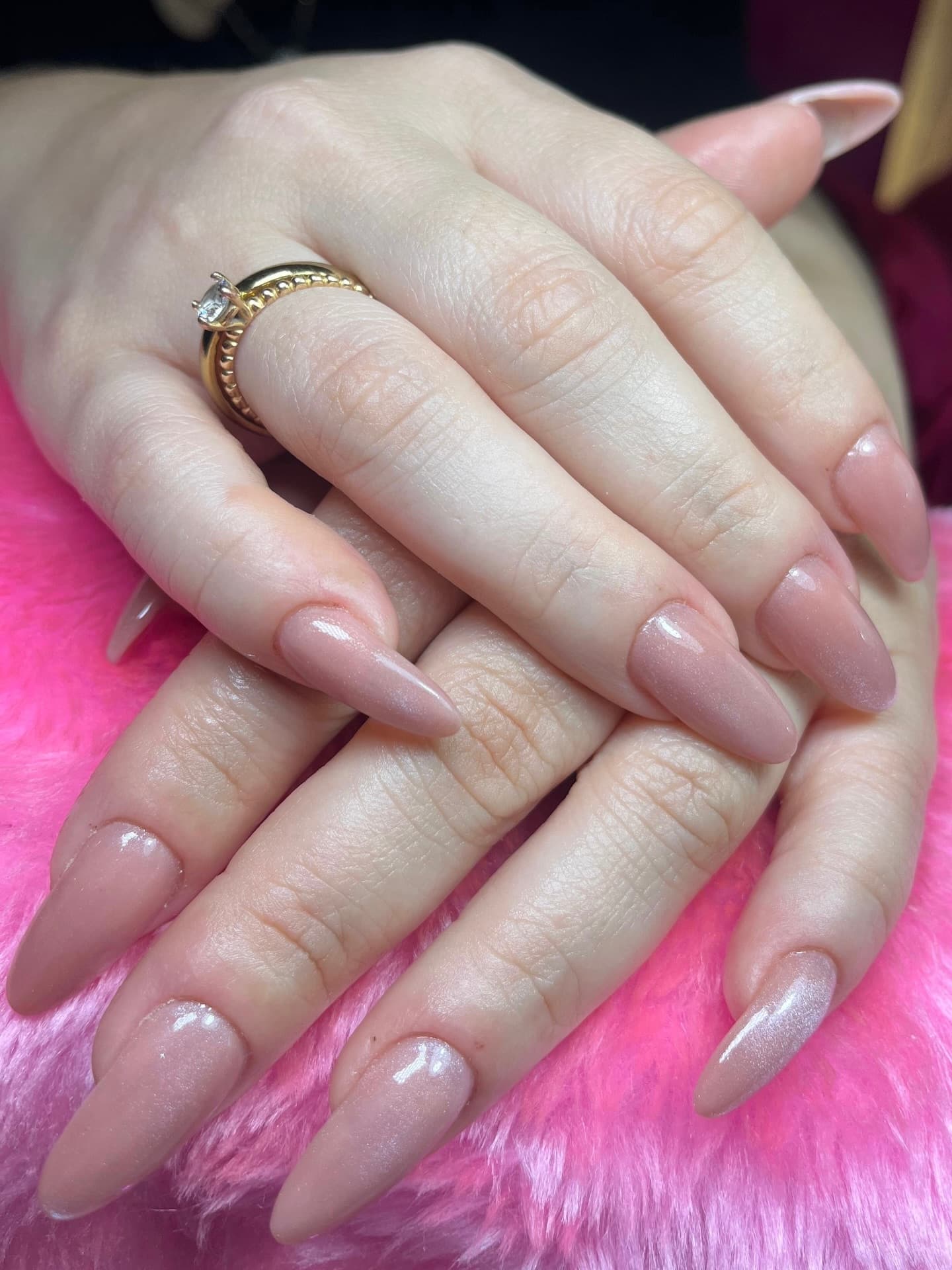 Nude almond nails with subtle shimmer and a metallic ring on the middle finger